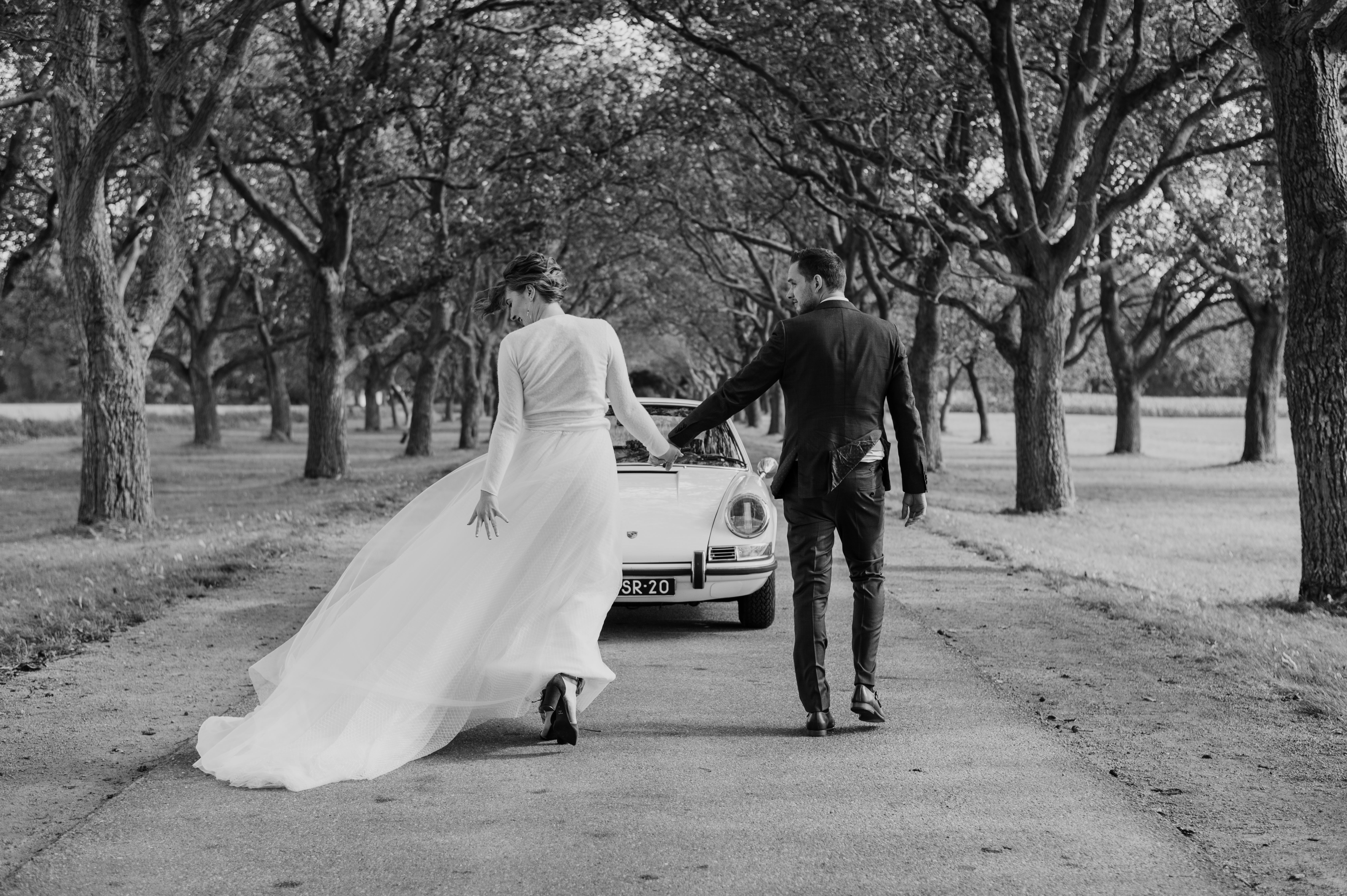 Wedding album art, couple walking down tree-lined path with vintage car